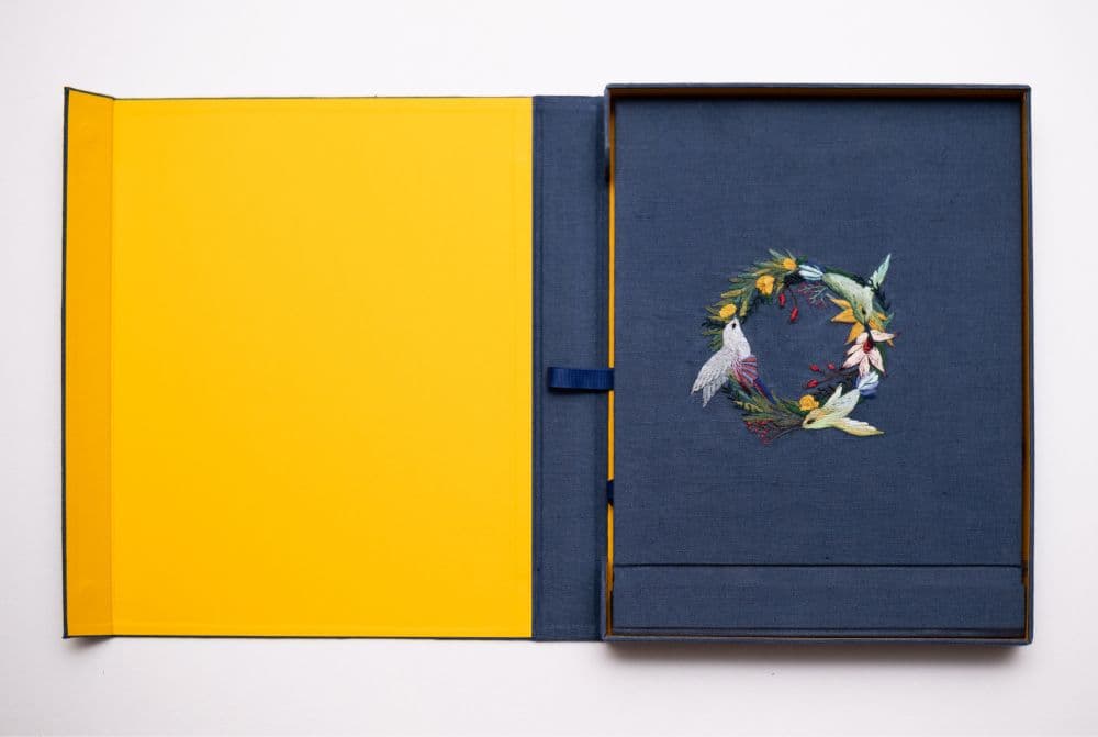 a hand-made photo album decorated with an embroidered design of a floral wreath with hummingbirds