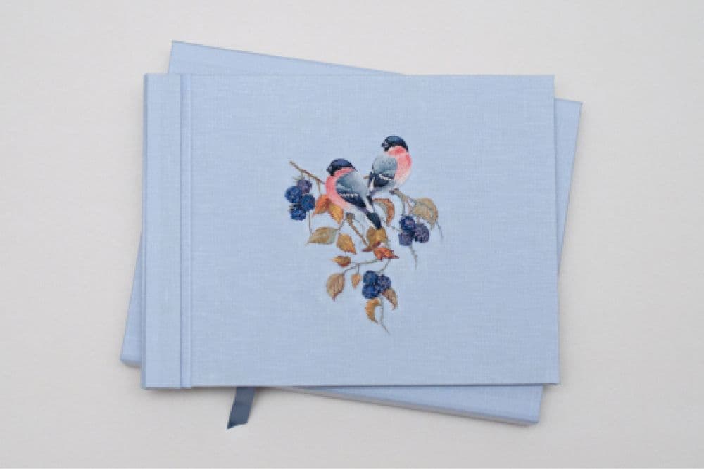 a hand-made photo album decorated with an embroidered design of two snowbirds