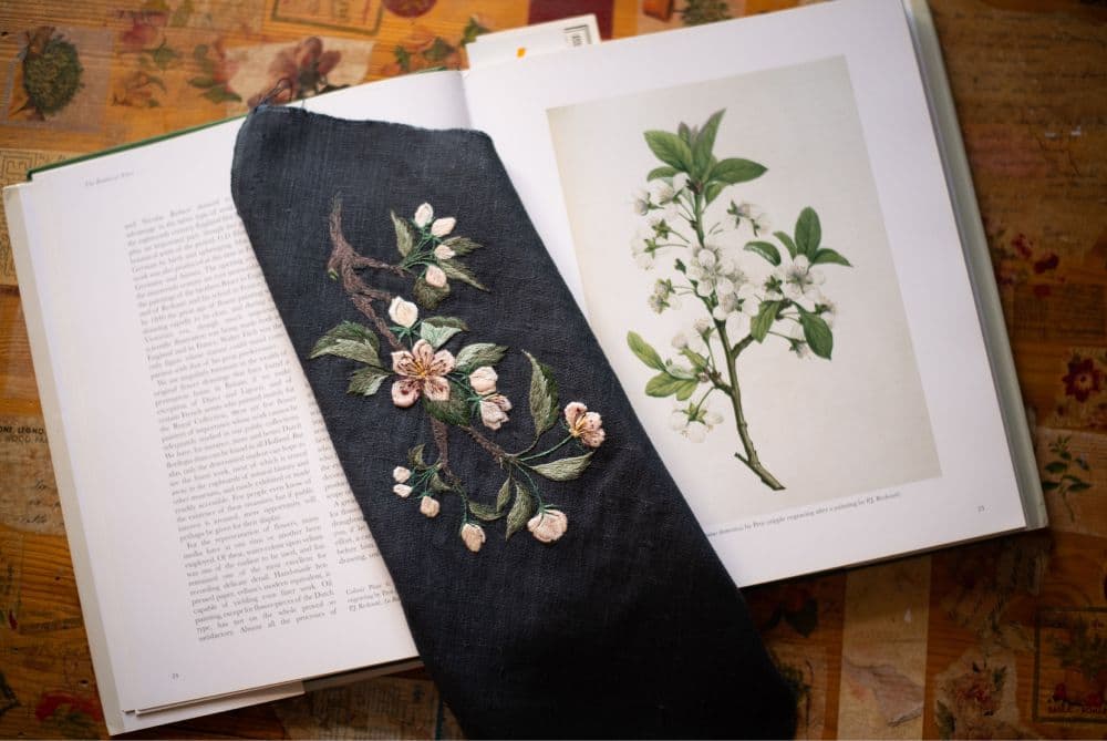 an opened book of botanical illustration with a piece of embroidered cloth