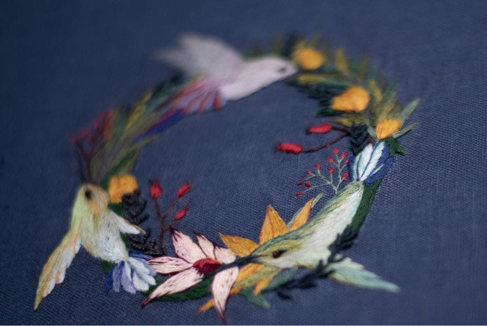 a close-up of a hand-made photo album decorated with an embroidered design of a floral wreath with hummingbirds