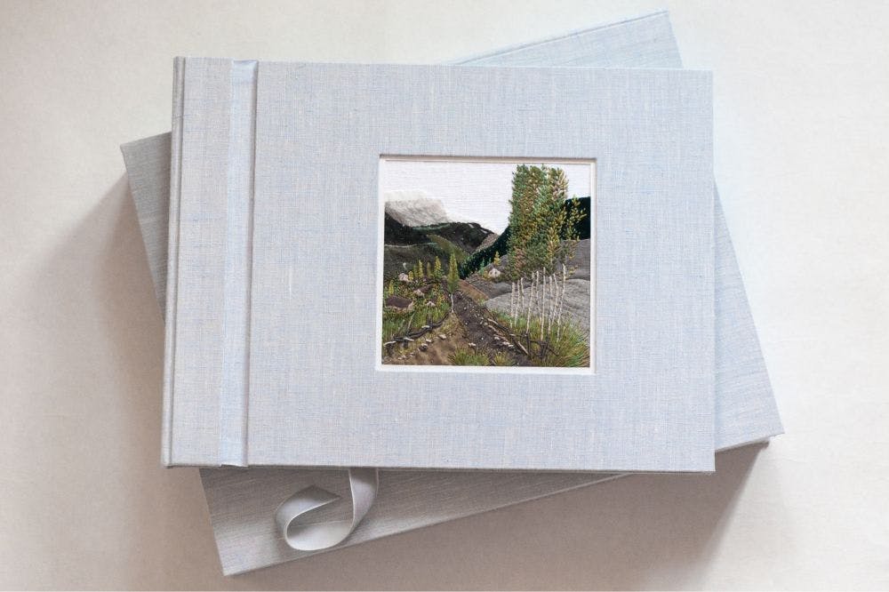 a cover of a hand-made photo album decorated with an embroidered design of a mountain view