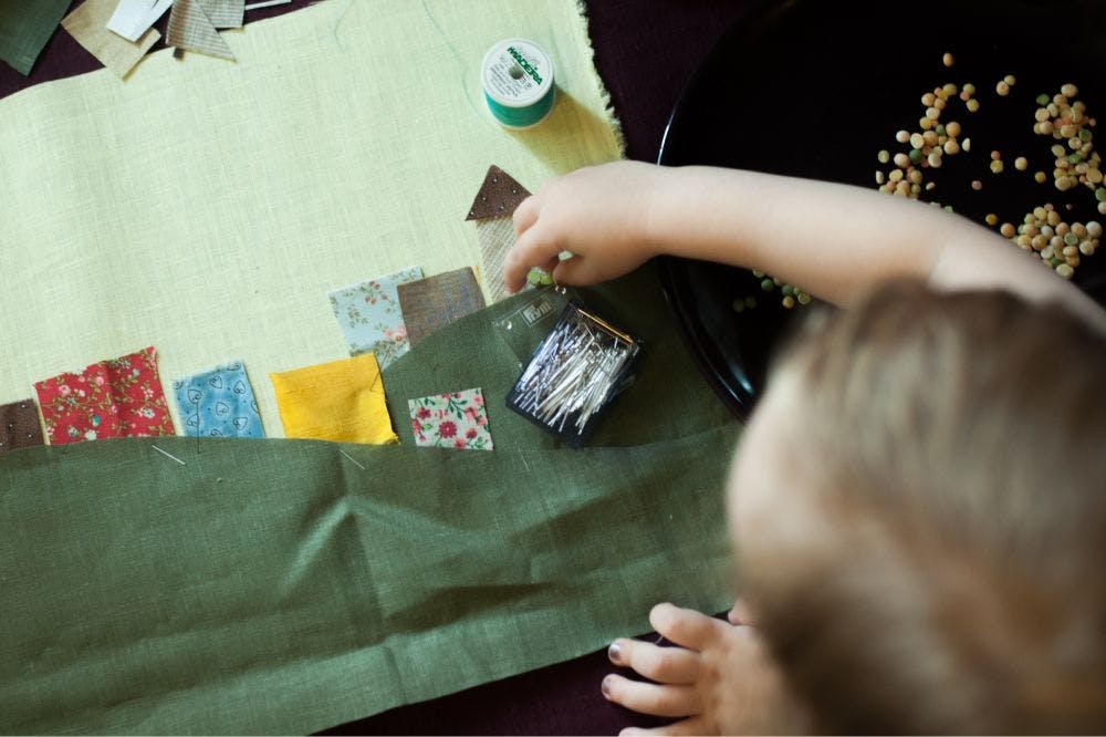 a child is playing with some shapes of textile craps making them look like houses and hills and countryside