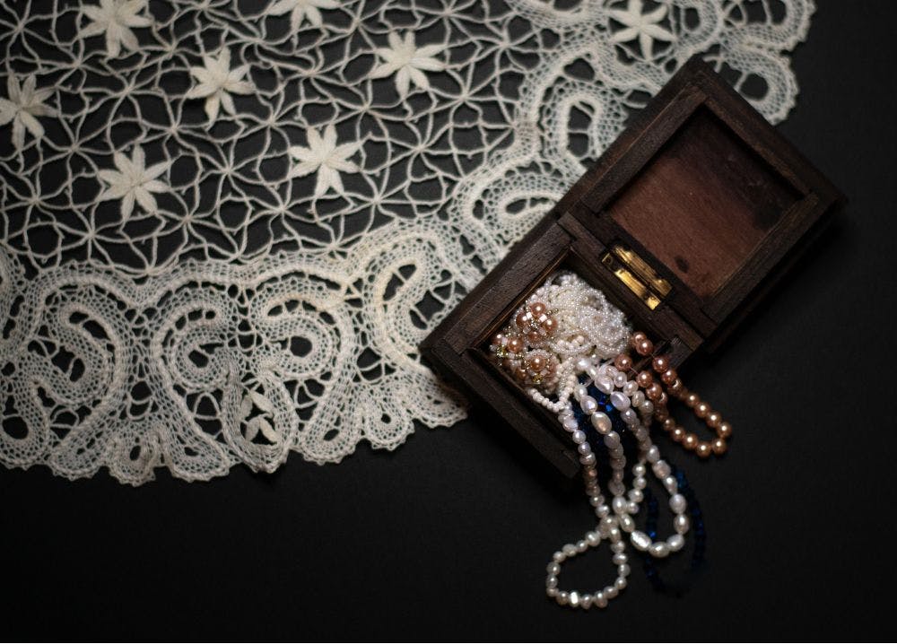 a piece of bobbin lace tablecloth and an old jewellery box are laying on the table