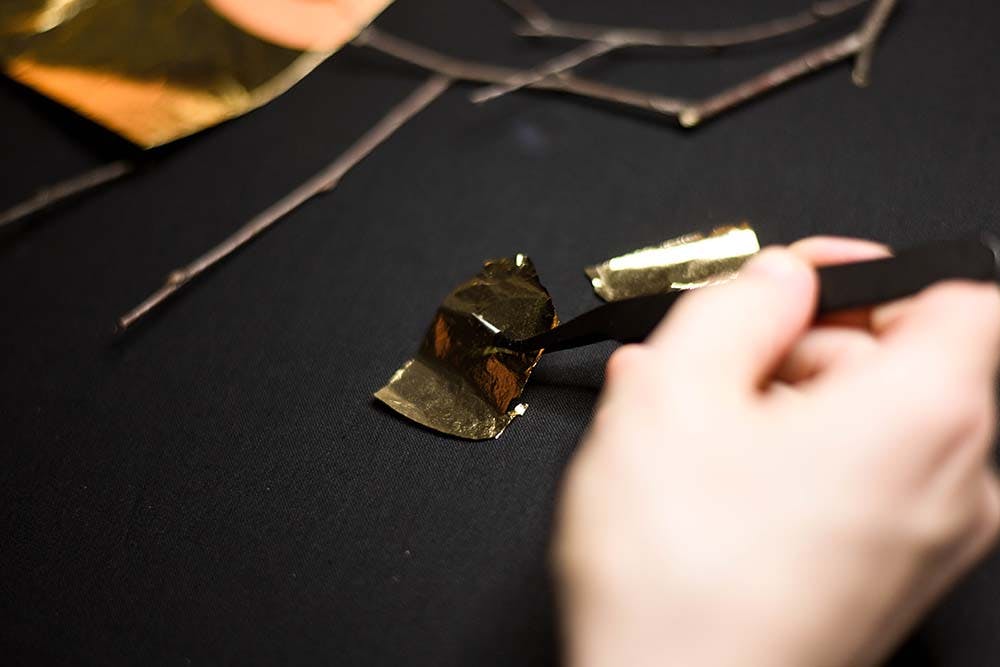 a hand is holding a piece of golden leaf to apply to the fabric