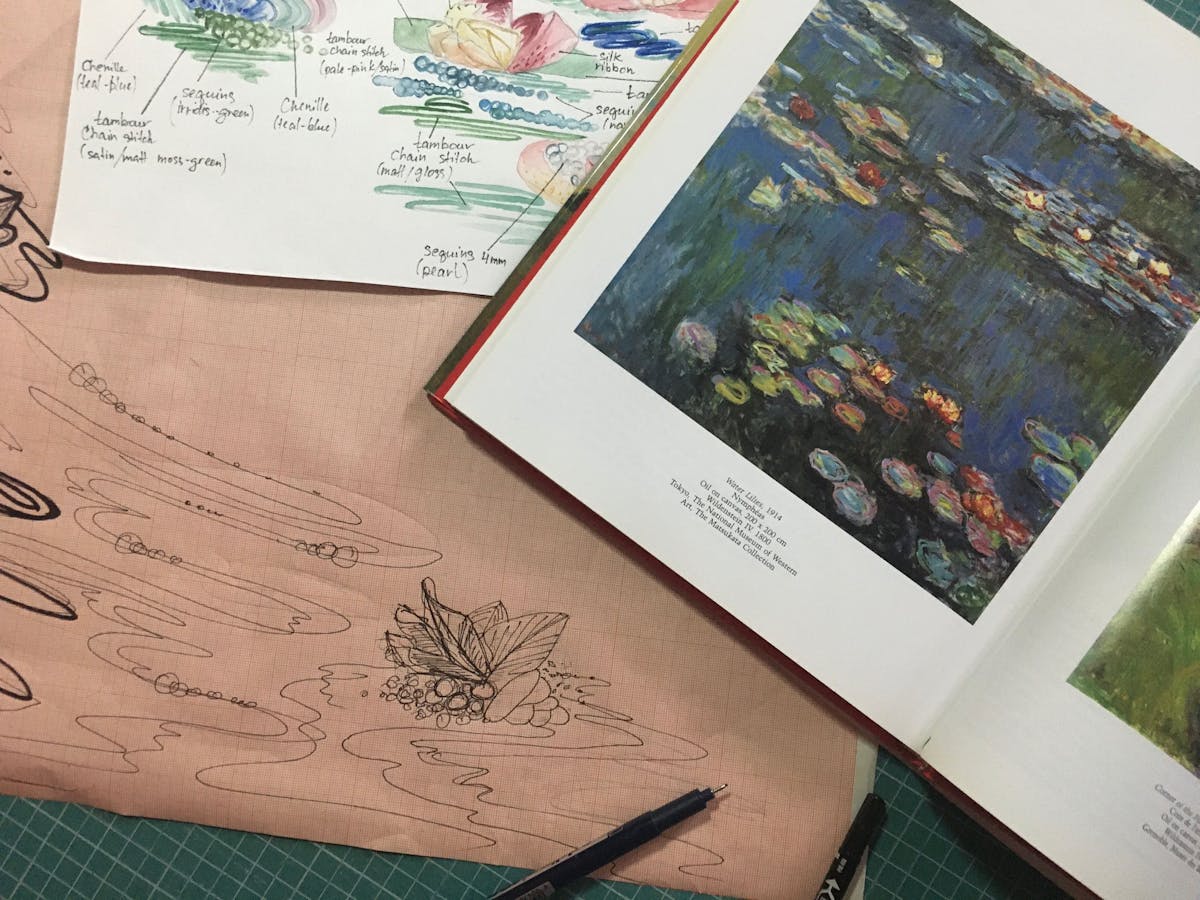 a close-up of the book displaying Monet's painting and the sketches of the embroidery
