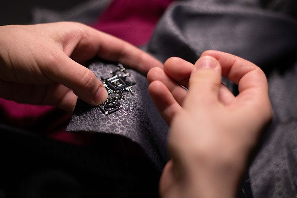 a pair of hands stitching, adding some glass beads to the design
